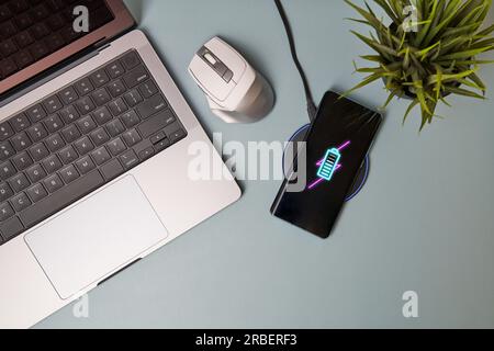 Charging mobile phone battery with wireless charging device on the table. Smartphone charging on a charging pad. Stock Photo
