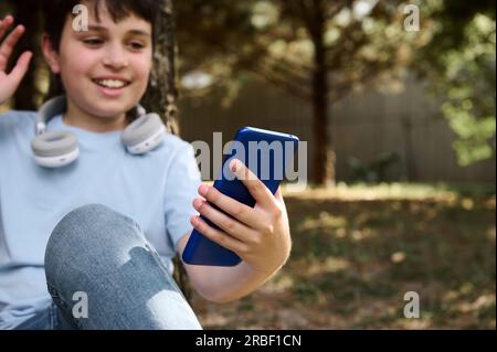 Selective focus on modern smartphone in the hand of a preteen boy talking via video link while resting outdoors. Kids. Online communication across the Stock Photo