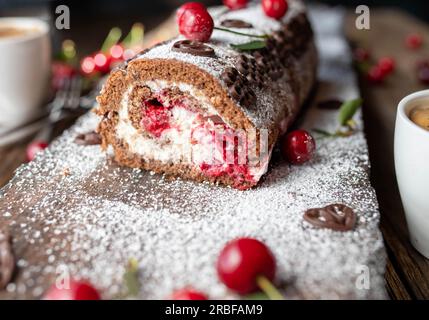 Chocolate cake with cherries and cream on wooden background. Black forest cherry swiss roll Stock Photo