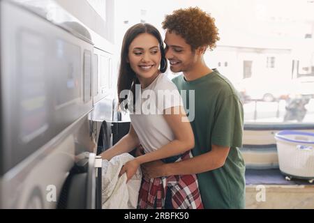 Romantic Man Hugging Wife Loading Washing Machine At Laundromat Room Stock Photo