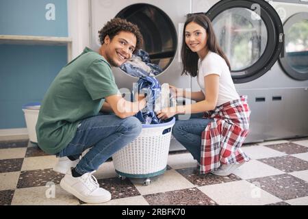 Happy Couple Doing Laundry Loading Washer Machine At Laundromat Room Stock Photo
