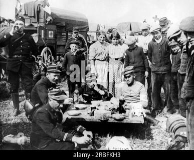 Argonne Forest, France:  November, 1918 French officers of an ambulance division dine by the side of the road with a German Red Cross prisoner who has fallen into their hands. A group of interested spectators has gathered around. Stock Photo