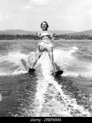 United States:  c. 1955 A young woman with a big smile on her face as she water skis close behind the boat. Stock Photo