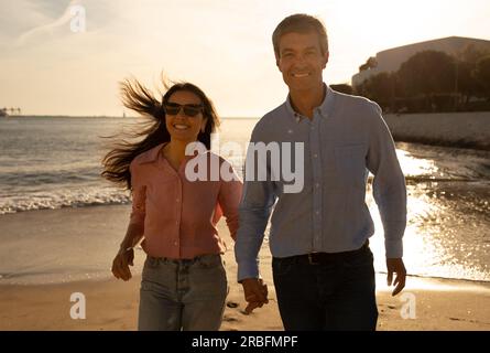 Happy mature couple running together on beach at sunset Stock Photo