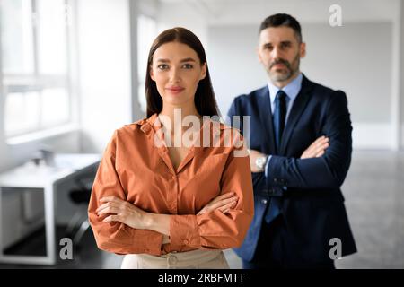 Two business leaders posing with folded arms and looking at camera, working together in office, selective focus on woman Stock Photo