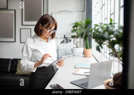 Freelancer lady working in office and using digital tablet, browsing business app, replying on emails online Stock Photo