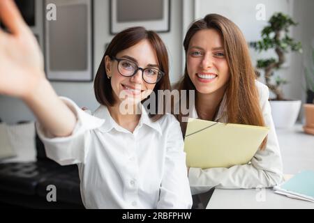 Two european female friends colleagues workers taking selfie, looking and smiling at camera during break in office Stock Photo