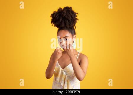 Serious strict confident millennial african american lady showing fists, fighting isolated on yellow background Stock Photo