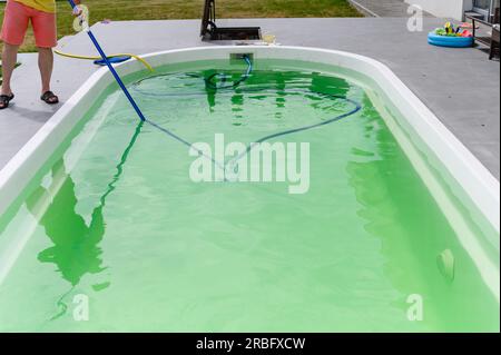 Man cleaning bottom of swimming pool by underwater vacuum cleaner Stock Photo