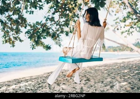 Carefree happy woman on swing on beautiful paradises beach. Relax and freedom concept Stock Photo