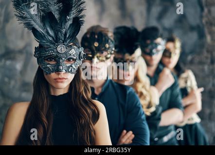 Group of people in masquerade carnival mask posing in studio. Beautiful women and men wearing venetian mask. Fashion, party, friends concept Stock Photo