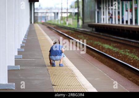 Little boy playing on the platform edge on railroad station. Safety on rails, travel in summer Stock Photo