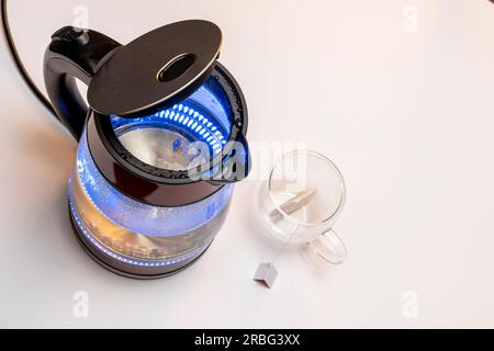 a new red modern boiling glass electric kettle with an open lid close-up with bubbling water and blue neon lighting. Slider shot Stock Photo