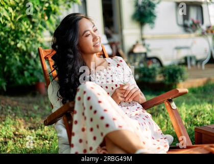 Beautiful young woman relax in chair during picnic beside her camper van. Rest, vacation, trip and holiday concept Stock Photo