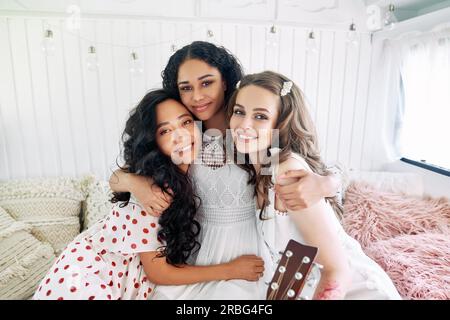 Three beautiful smiling girl friends hugging each other in a close embrace. Multi-ethnic beauty. Different ethnicity women - Caucasian, African, Asian Stock Photo