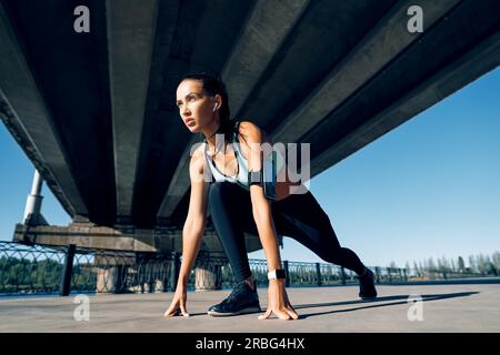 Runner woman ready to run in running start pose on the city industrial background. sprinter training outdoor Stock Photo