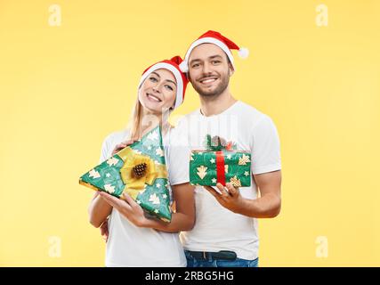 Young happy couple with xmas gift boxes over yellow background. Present, holiday, celebration concept Stock Photo