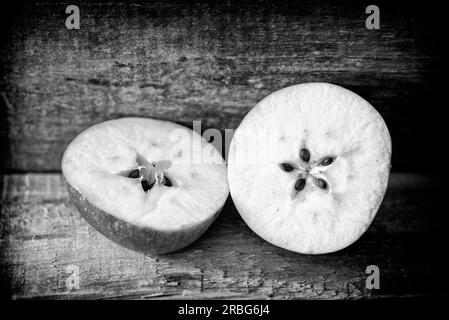 Cut apple on a wooden plank, showing the seeds in a delicate five pointed star motive. Black and white photo Stock Photo