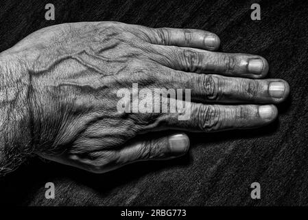 Black and White photo of a senior man left hand on dark background Stock Photo