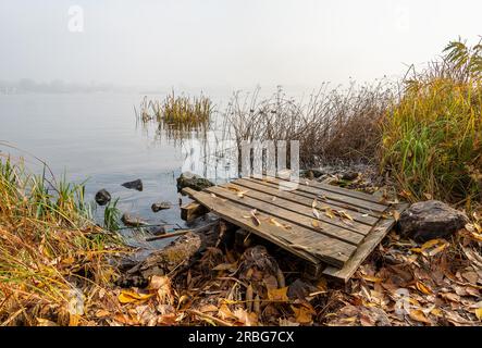 A wooden pontoon over big stones close to the blue Dnieper river is waiting for the fisherman Stock Photo