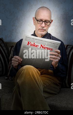 A man wearing glasses is sitting on a couch at home, reading a newspaper reporting fake news. Fake Lorem ipsum text Stock Photo