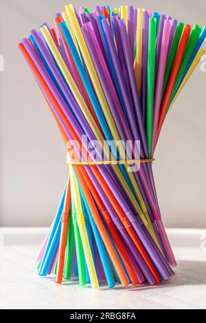a lot of bright multicolored cocktail tubes are clamped with an elastic band in a bundle on a white background. Multicolored Plastic Cocktail Tubes Stock Photo