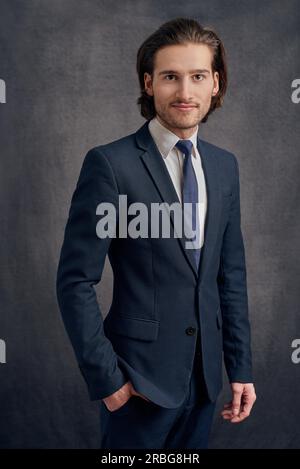 Handsome young man with long haircut in business suit with blue necktie, standing and looking at the camera Stock Photo