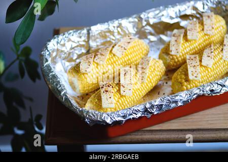 Raw corn on cobs with butter slices and spices in baking dish. Preparing corn for cooking. Vegetable season. Fresh corn cobs ready to cook baked corn Stock Photo