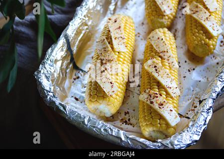 Raw corn on cobs with butter slices and spices in baking dish, close up. Preparing corn for cooking. Fresh corn cobs ready to cook baked corn with but Stock Photo