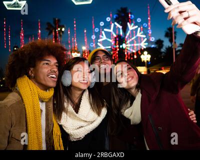 Group of multiethnic friends making a selfie and having fun in a city street during a winter night. Stock Photo