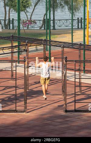 Ukraine, August 31, 2018, A muscular young man is doing chin-ups on the bar. He uses the sports equipment available to the public in Natalka Park Stock Photo