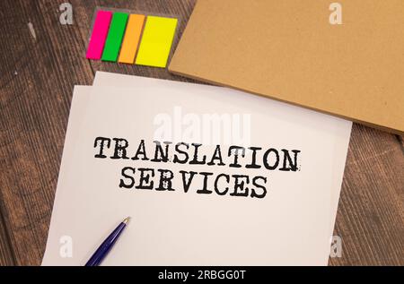 On a light background, gold-framed glasses, a flower in a pot, a green notebook, a red pen and a brown notebook with the text TRANSLATION SERVICES. Bu Stock Photo