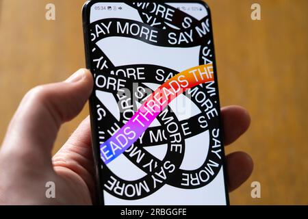 Man's hand holding a smartphone showing Instagram Threads app loading startup page with the 'Say More' tag line and Threads graphic background Stock Photo