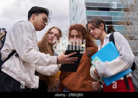 Group of students sharing an digital tablet to check internet standing up outside the campus Stock Photo