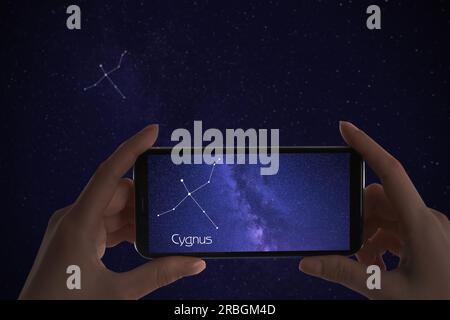 Woman using stargazing app on her phone at night, closeup. Identified stick figure pattern of Swan (Cygnus) constellation on device screen Stock Photo