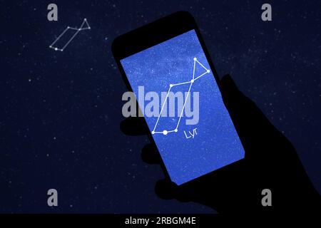 Woman using stargazing app on her phone at night, closeup. Identified stick figure pattern of Lyra constellation on device screen Stock Photo