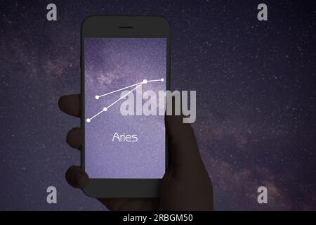 Woman using stargazing app on her phone at night, closeup. Identified stick figure pattern of Aries constellation on device screen Stock Photo