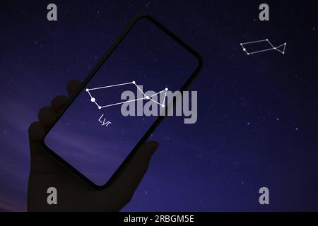 Woman using stargazing app on her phone at night, closeup. Identified stick figure pattern of Lyra constellation on device screen Stock Photo