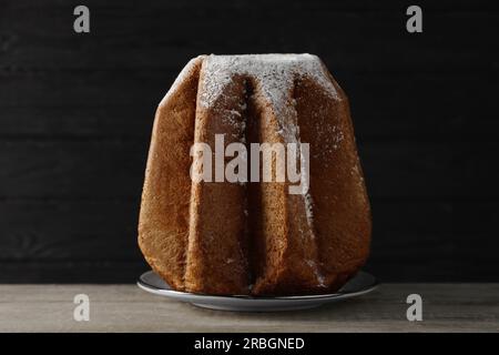 Delicious Pandoro cake decorated with powdered sugar on wooden table against black background. Traditional Italian pastry Stock Photo