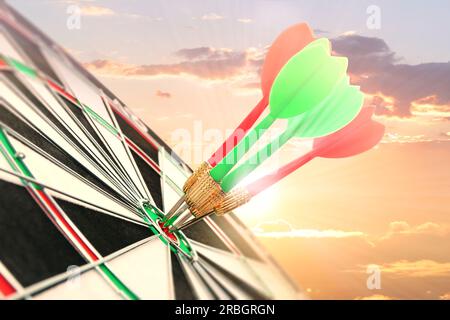 Dart board with color arrows hitting target against sunset sky Stock Photo