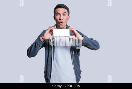 A surprised guy shows a blank screen of a smartphone. Amazed young man showing an advertisement on a cell phone. Surprised handsome man showing the ho Stock Photo