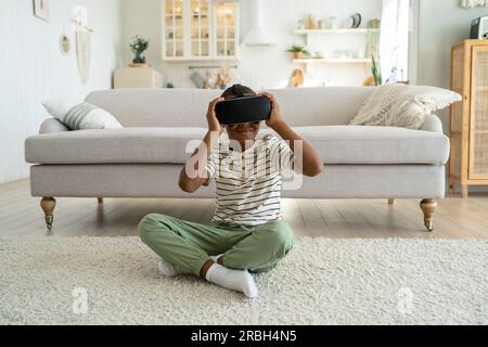 African American boy child sitting on floor at home using virtual reality device watching 3d video Stock Photo