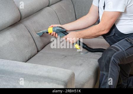 Dry cleaner's man employee removing dirt from textile furniture in flat. closeup, vacuum clean sofa Stock Photo
