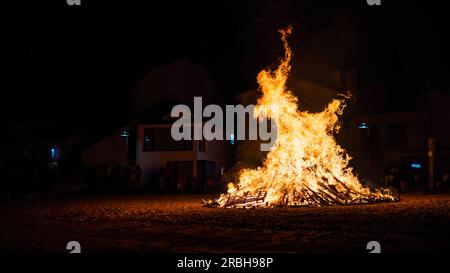 rural celebration with the hole town watching the fire of a bonfire at the beach at night Stock Photo
