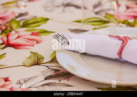 Elegantly table set at wedding, christening banquet. Floral tablecloth with pink flowers and white round plate, napkins. Thanksgiving holiday dinner d Stock Photo