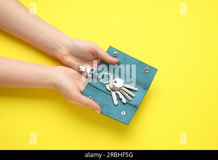 Woman holding open leather holder with keys on yellow background, top view Stock Photo