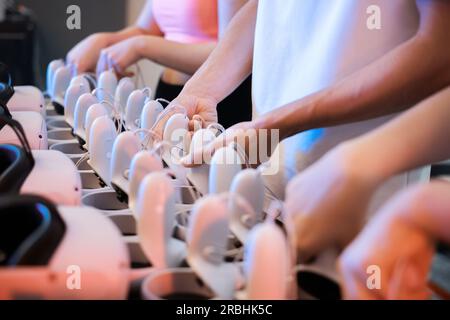 Virtual reality VR equipment on a table. Playmates choosing VR headsets and joysticks. Neon lights Stock Photo