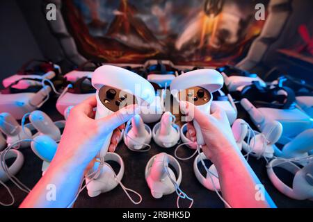 First person view of choosing virtual reality VR equipment from a table. VR headsets and joysticks. Neon lights Stock Photo