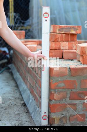 A mason person is using a spirit level to check  house brick wall foundation. Brick house wall foundation with bitumen waterproof barrier. Stock Photo