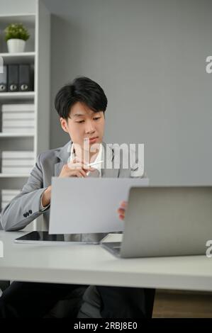 A smart and focused Asian businessman or male boss reading a document at his desk in the office. Stock Photo